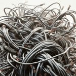 The image shows a chaotic tangle of numerous electrical cables. The cables are intertwined in a dense, disorganized mass, with many ends frayed and exposing copper wires. The overall scene conveys a sense of disorder and complexity, highlighting the intricate network of wires and their damaged insulation. This image represents the need for electrical service upgrades.