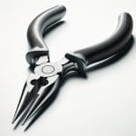 A close-up image of a pair of needle-nose pliers with black ergonomic handles. The pliers are positioned on a white background, showcasing their sleek, metallic jaws and the detailed texture of the handles. The image emphasizes the tool's precision and design, highlighting its functionality and modern appearance.